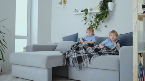 Two-boys,-4-and-2-years-old,-are-watching-TV-sitting-on-the-couch.-An-exciting-TV-show.-View-cartoons.-Children-watch-an-exciting-TV-show.